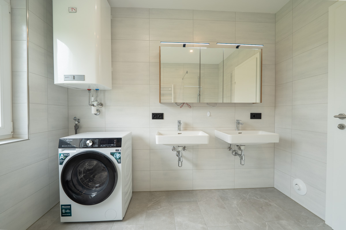 Modernes Badezimmer mit Doppelwaschbecken, Waschmaschine und Warmwasserspeicher nach Badsanierung